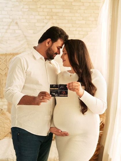 A sweet moment of anticipation, with a couple looking at their baby's sonogram pictures together. They are framed by the soft light of a window in a cozy, boho-styled room.