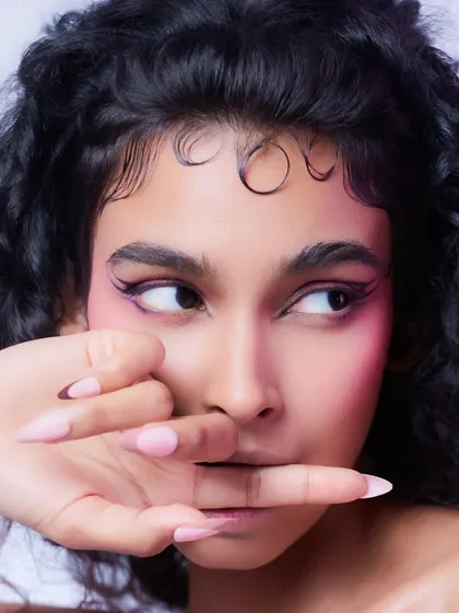 A playful beauty close-up with a focus on the eyes and nails. The lighting is clean and bright, emphasizing the sharp eyeliner and styled baby hairs.
