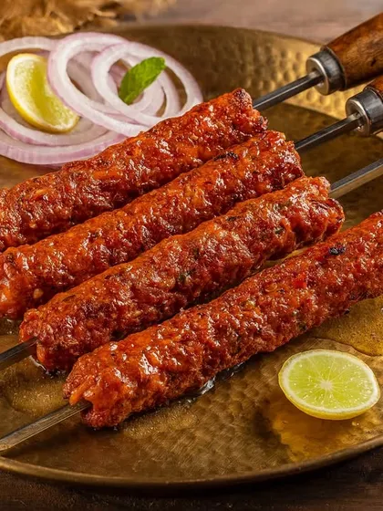 Juicy mutton seekh kebabs on skewers, garnished with onion rings and lemon. This shot for Nazeer Foods highlights the char and texture of the grilled meat.