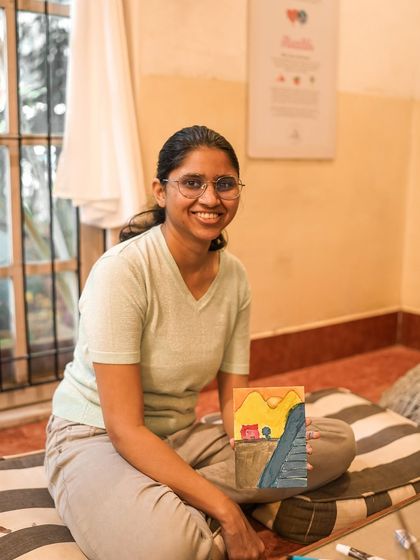 A smiling participant holds up her finished painting, happy with her creative work.