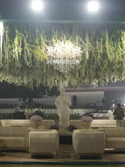 A luxurious lounge area with plush white sofas, set under a ceiling of hanging white flowers and a crystal chandelier.