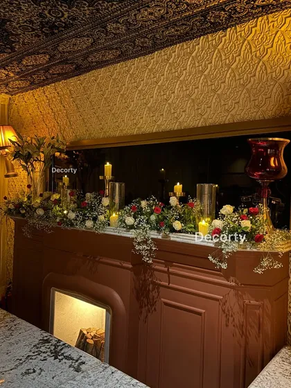 A beautifully decorated fireplace mantel, adorned with a lush floral garland and candles, adding a warm and romantic touch to the anniversary party venue.