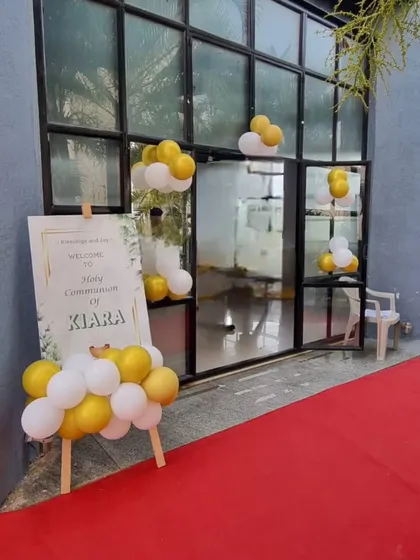 The entrance to a Holy Communion ceremony, with a personalized welcome sign and a simple white and gold balloon arrangement.