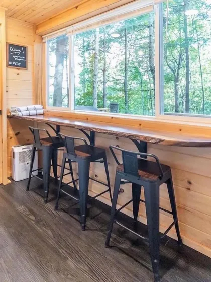 The interior of this container home features a cozy breakfast bar with a large window overlooking the forest. The natural wood finish creates a warm and inviting atmosphere, perfect for enjoying a morning coffee.