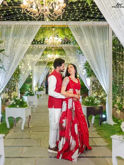 We love creating magical settings for your sangeet or reception. This couple is framed by a romantic walkway of draped white fabric, sparkling fairy lights, and elegant chandeliers, perfect for an evening of dance and celebration.