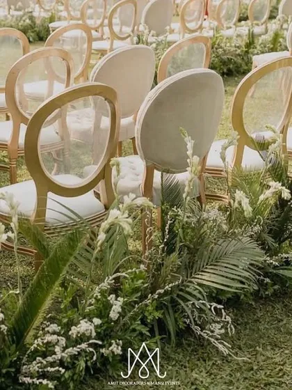 The aisle is defined by rows of transparent-backed chairs and bordered with lush, low-lying arrangements of ferns and white flowers, creating a garden path feel.