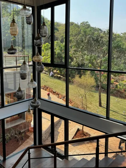 A detail of the cascading light fixture in the double-height space of the 6AM House. The lights hang like delicate glass drops against the backdrop of the green landscape seen through the large windows.