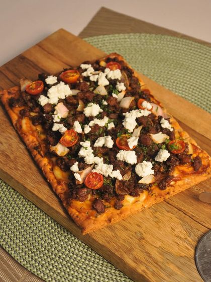 A rustic minced meat flatbread topped with fresh feta cheese and cherry tomatoes. Served on a wooden board, this appetizer is a hearty and flavorful option for guests who appreciate bold, savory tastes.