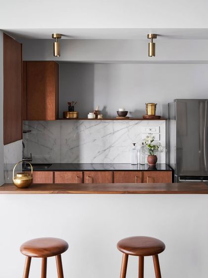 A custom kitchen with a breakfast bar. The cabinetry is made from warm wood with a marble backsplash, demonstrating my approach of mixing natural materials for a timeless look.