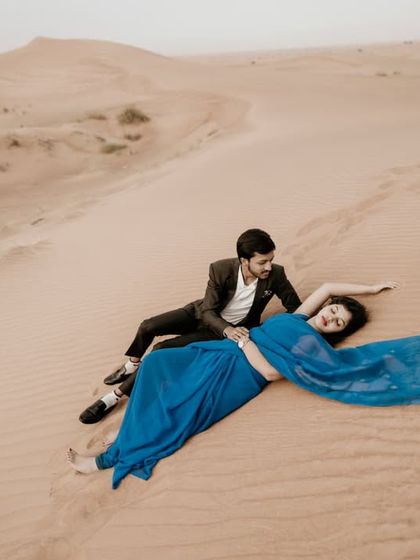 A dramatic and artistic pose in the desert, with the bride's long blue fabric trailing in the sand.