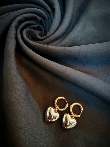 The 18k gold plated classic retro heart earrings, shot against a rich, dark fabric to highlight their shine.