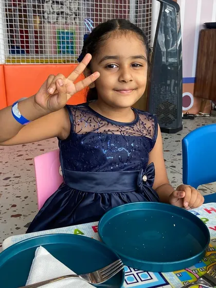 A happy guest at Sarth's Paw Patrol themed birthday party. She's all smiles, sitting at one of our alphabet-themed tables, ready to enjoy the party food after a fun time in the play area.