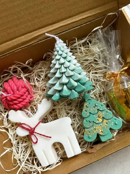 A curated Christmas gift box filled with various festive soy candles, including a reindeer, Christmas tree, and a ball of yarn.