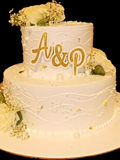 A timeless two-tier wedding cake that exudes elegance. Featuring classic white frosting with subtle texturing, delicate white roses, baby's breath, and personalized gold monogramming, this cake is perfect for celebrating your special day.