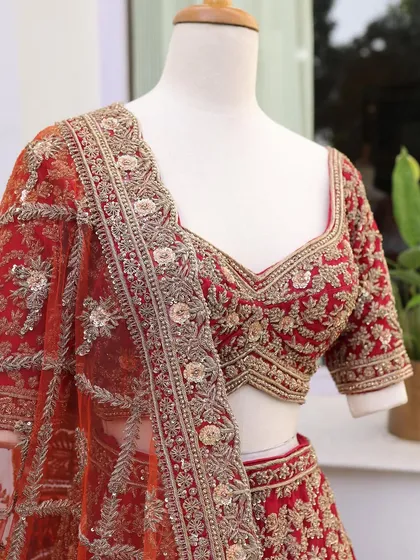 A close-up of a classic red bridal blouse with delicate floral embroidery. This shot highlights the fine zardozi and threadwork.