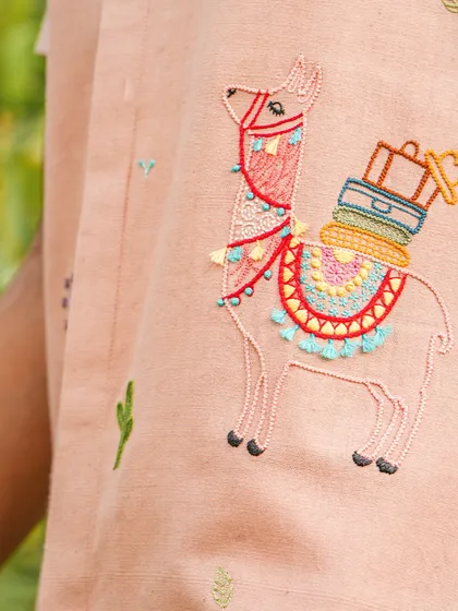 A close-up of the star of the show: the hand-embroidered llama, complete with a colorful saddle and luggage. This playful detail makes the shirt a truly unique piece, tailored to your personality.