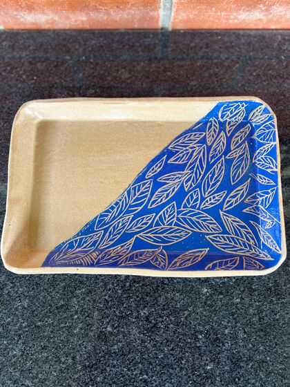 A rectangular tray with a beautiful sgraffito leaf pattern etched into a deep blue background. This is perfect for serving snacks, as a trinket dish, or as a decorative piece.