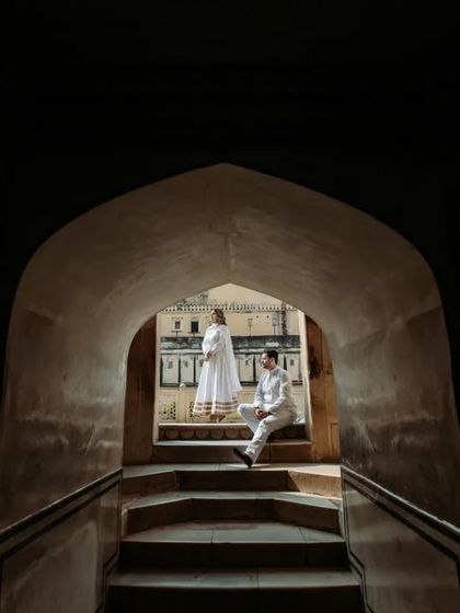Using the contrast of light and shadow to create a dramatic, artistic portrait. The couple is framed within a dark archway, looking out into the bright courtyard of a palace.
