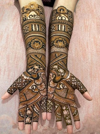 A beautiful example of full-arm bridal mehandi with matching peacock designs on both hands, showcasing symmetry and intricate filler patterns.