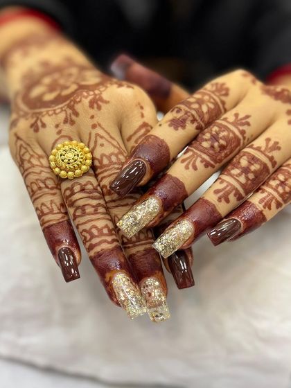 A stunning example of bridal nail art. The rich brown polish is paired with dazzling gold glitter extensions, perfectly complementing the intricate henna design for a complete and regal bridal look.