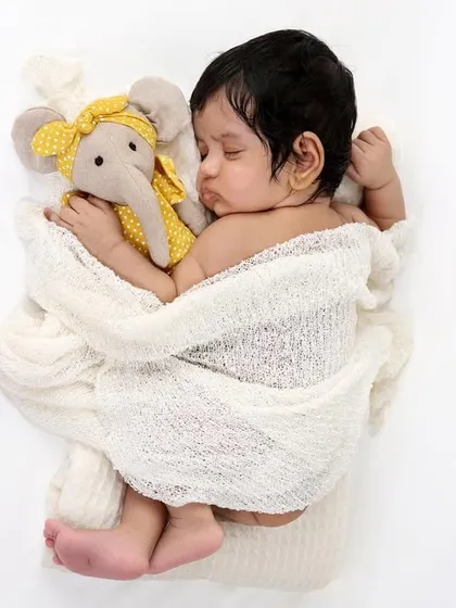A sweet newborn cuddling with a small elephant toy. The simple white background emphasizes the baby's innocence and the tender moment.