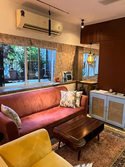 This view shows the comfortable seating area with a mix of textures and colors. The custom light blue cabinet with cane doors adds a unique touch to the room's decor.