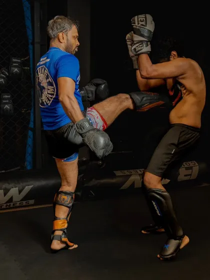 A fighter executes a body kick during a sparring session, while the coach observes and absorbs the blow.