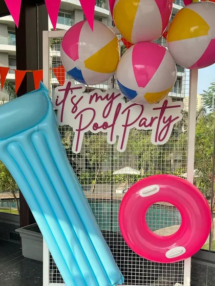 A fun photo spot for a pool party, featuring a neon sign, inflatable mattress, and beach balls.