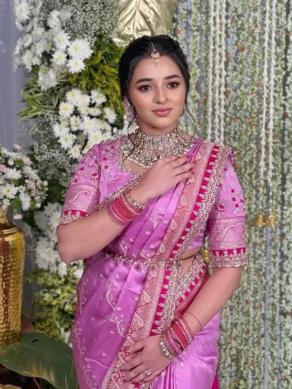 The client stands against a floral backdrop, her traditional pink saree and elegant makeup taking center stage.