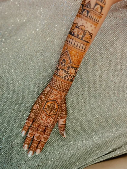 A close-up of the back of the hand and forearm, highlighting the lotus motifs and intricate filler patterns.