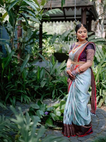 A full-length view of the bride in her pastel blue and maroon saree, posing in a garden. The colors look beautiful in the natural light.