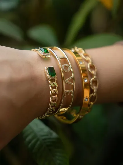 A close-up of our emerald and love cuff bangles stacked together. The combination of the green stones with the classic gold "LOVE" design is effortlessly elegant.