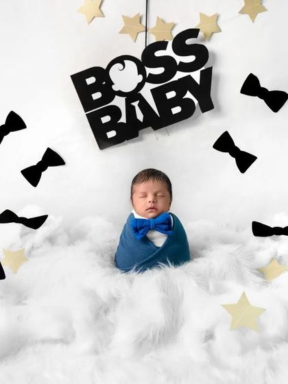 A classic "Boss Baby" shot, with the newborn swaddled in blue and sleeping on a bed of clouds. This theme is always a hit with parents.
