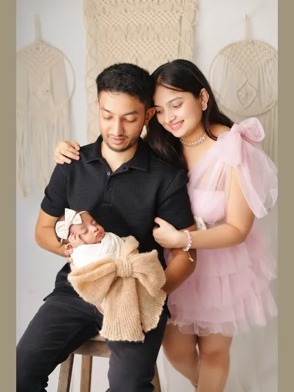 A full-length family portrait showing the parents with their newborn. The mother's pink dress adds a soft touch of color to this beautiful photo.