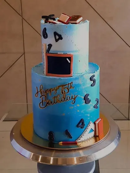 A full view of the two-tier Swiss Chocolate cake for a teacher's 75th birthday, showcasing the blue ombre and educational-themed decorations.