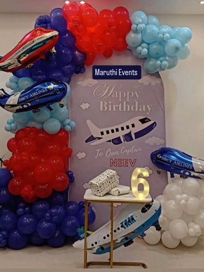 An airplane-themed party for a future captain. The setup includes a custom backdrop, airplane foil balloons, and balloon clouds in red, white, and blue.