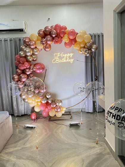 This is a duplicate of ID 17, 49, 92, 186, 209. An elegant balloon ring decoration for an intimate home celebration. This setup features a half-arch of chrome and pastel balloons on a golden ring, with a 'Happy Birthday' neon sign.