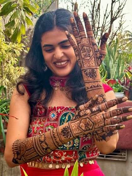 A smiling client with her intricate mehndi. The design includes a mix of jaal patterns, floral motifs, and personalized elements.