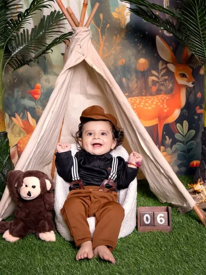 Celebrating a six-month milestone with a jungle explorer theme. The setup includes a tent, a toy monkey, and a wooden block indicating the baby's age, all on a grassy mat.