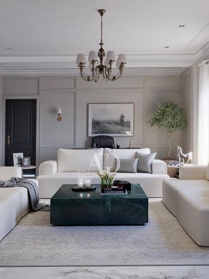 An example of "soft minimalism" where classical principles are applied with a restrained hand. The room features clean, modern sofas and a striking green marble coffee table, all framed by traditional wall paneling and a classic chandelier.