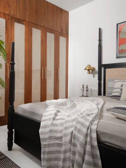 The primary bedroom features a custom four-poster bed in a dark finish, creating a striking contrast with the white walls. The wardrobe doors are detailed with wood and fabric panels.