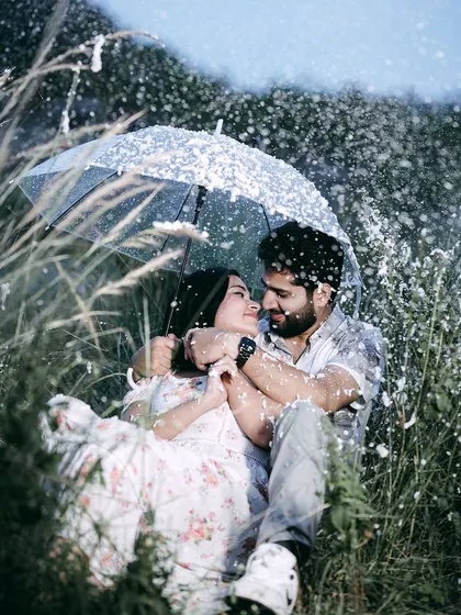 A cozy and magical pre-wedding moment, with a couple huddled under an umbrella amidst a flurry of artificial snow, creating a dreamy and intimate atmosphere.