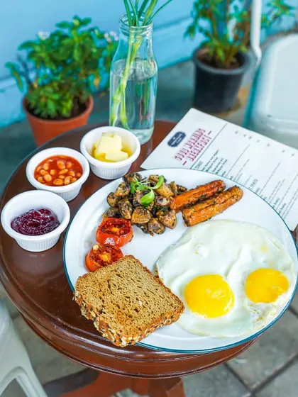 A classic American breakfast with sunny-side-up eggs, toast, baked beans, and grilled tomatoes. The bright, outdoor lighting gives it a fresh and wholesome feel.