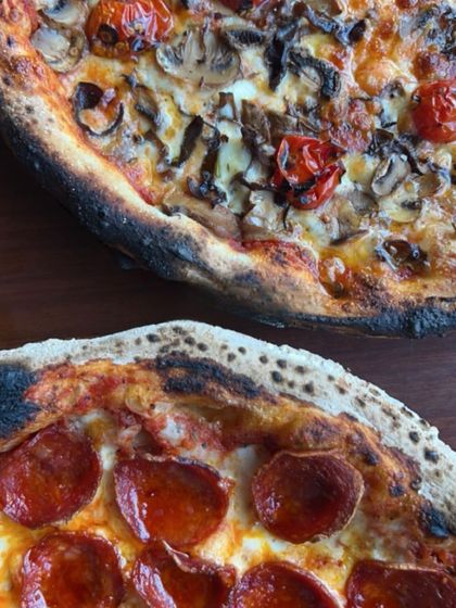 A close-up of two of our favorites: a classic pepperoni and a gourmet mushroom pizza with roasted cherry tomatoes. Notice the perfectly charred, airy crust that's a hallmark of our wood-fired oven.