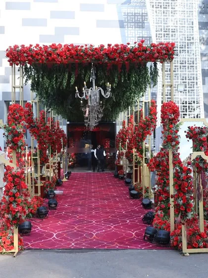 This grand red carpet entrance was designed to make a statement. The walkway is lined with towering arrangements of red roses, leading to a canopy of lush greenery and sparkling chandeliers.