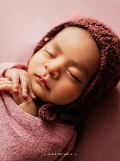 A close-up of another pink setup, this time with a cozy knitted bonnet. The focus is on the baby's serene, sleeping face.