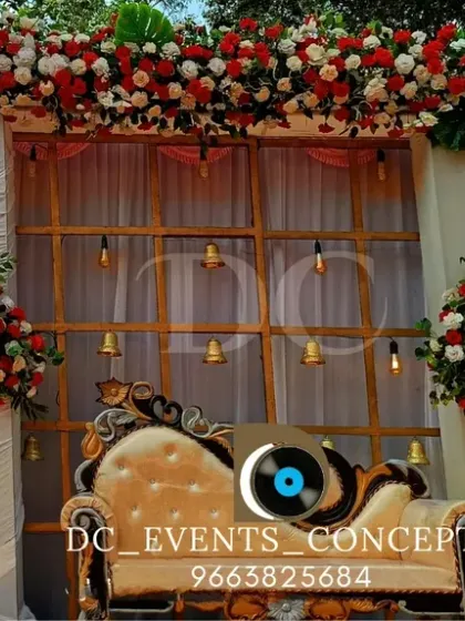 A beautiful outdoor Mehendi stage setup with a backdrop of red and white florals. The elegant draping and hanging bells add a traditional touch to the bright and airy design.
