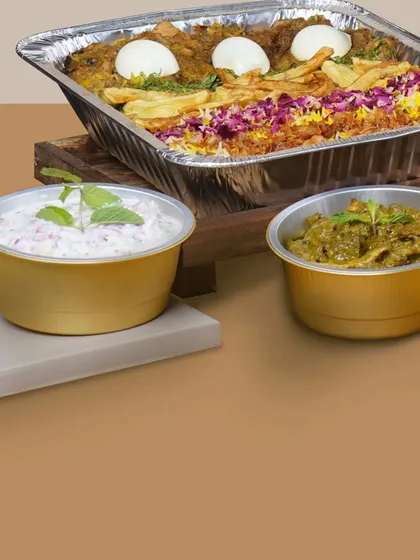A beautifully arranged bulk order featuring a tray of biryani, Dahi Cachumar, and Mutton Pahadi Keema, ready for a family celebration.
