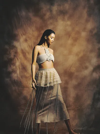 A full-length shot showcasing a conceptual look with a wet-hair effect and bronzed, glowing skin for a raw, elemental vibe.