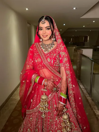 Whispers of tradition, echoes of elegance. This stunning Indian bride is wearing a classic red lehenga, and the makeup is designed to enhance her features with a soft glow and defined eyes.